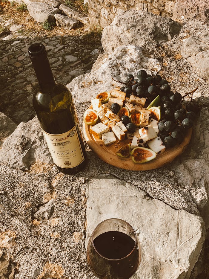 A rustic setup of wine and a cheese platter with figs and grapes on a stone surface outdoors.