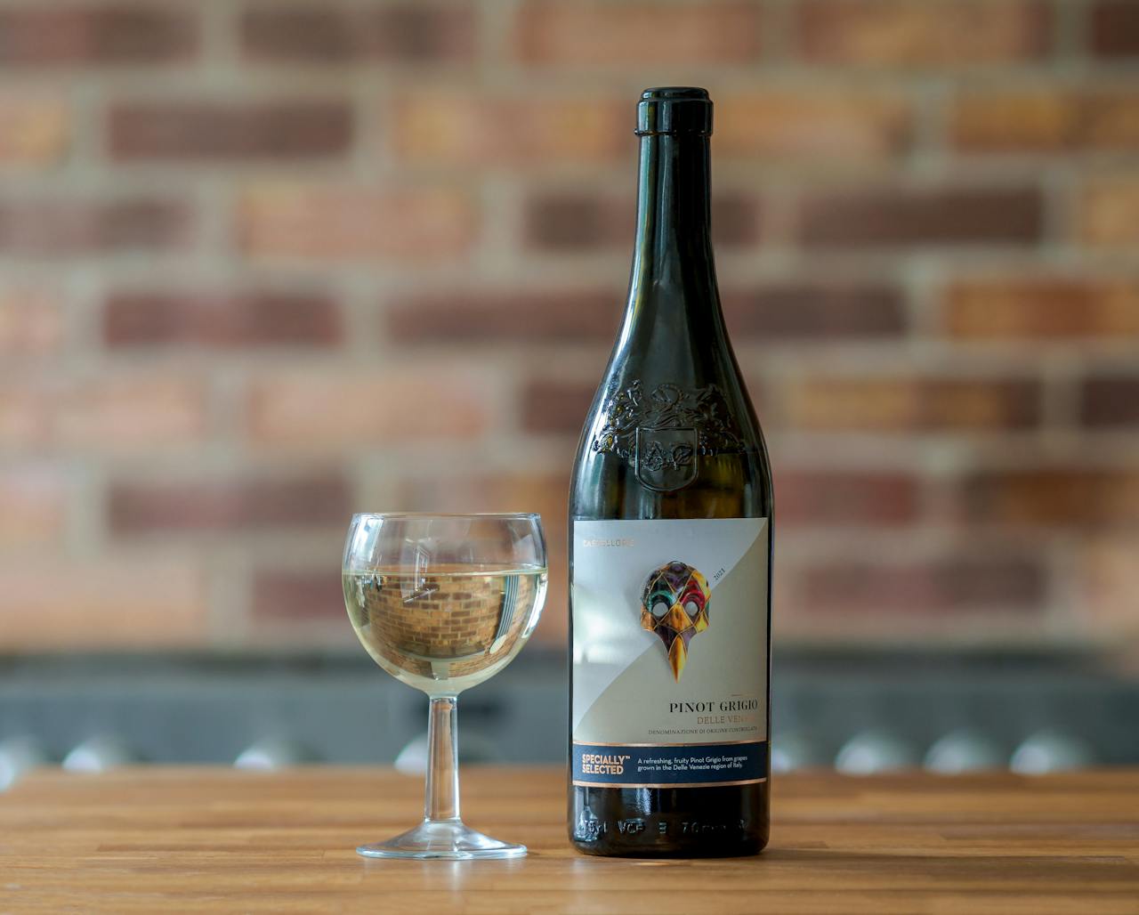faq-img Elegant Pinot Grigio bottle and wineglass on a wooden table against a brick wall.